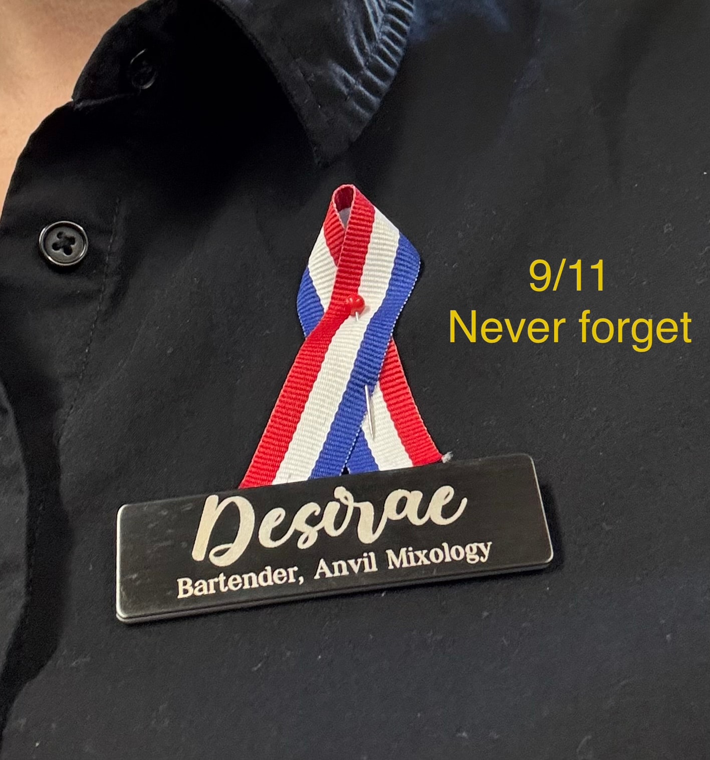 Desirae wearing her Anvil Mixology name badge with a red, white, and blue 9/11 remembrance ribbon — Never Forget