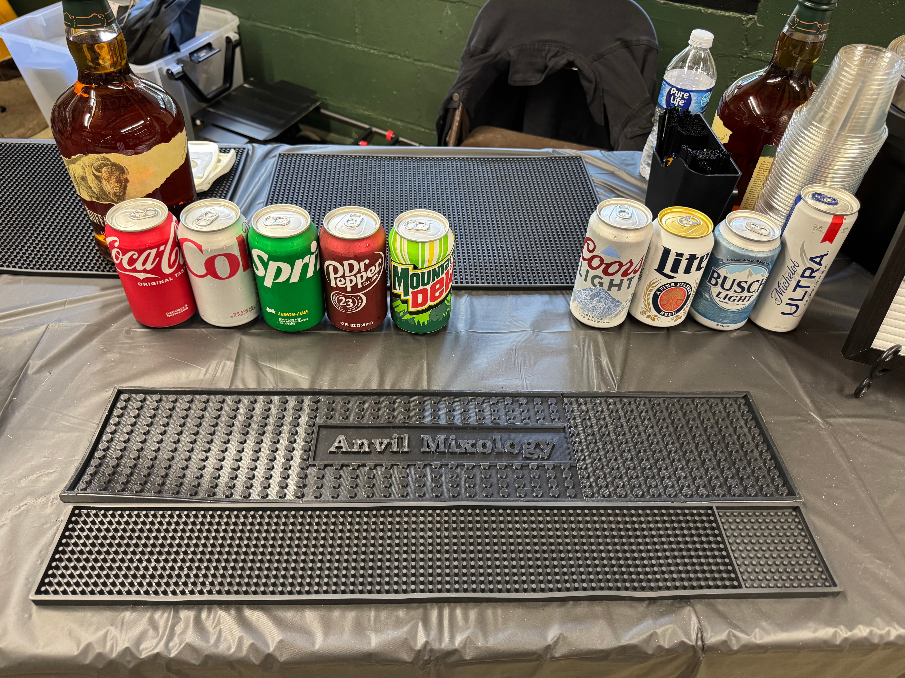 Anvil Mixology branded bar mat with assorted soda cans and beer cans lined up at the Sporting Clays for Scouting event