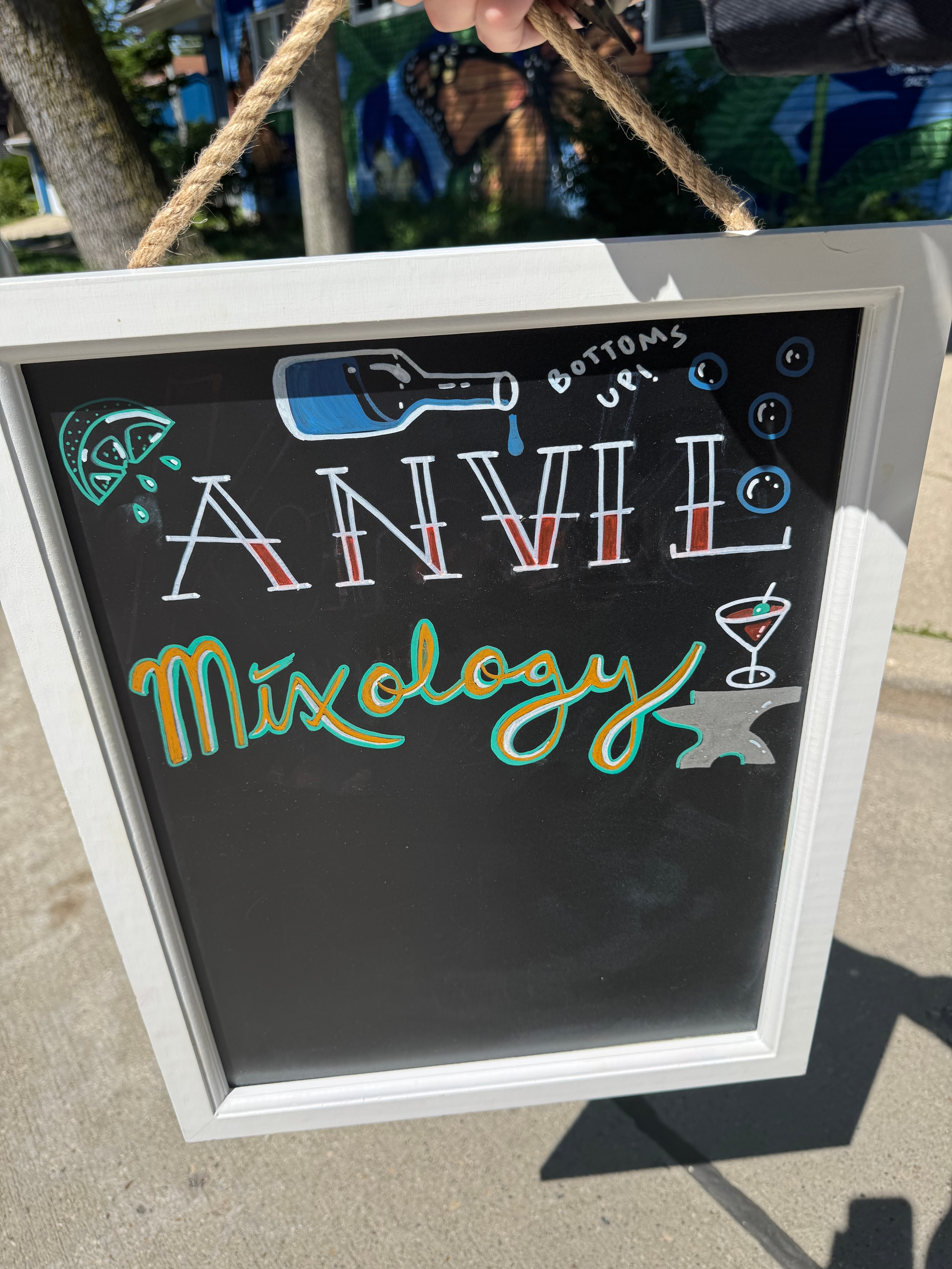 Anvil Mixology hand-drawn chalkboard sign with cocktail illustrations displayed outdoors
