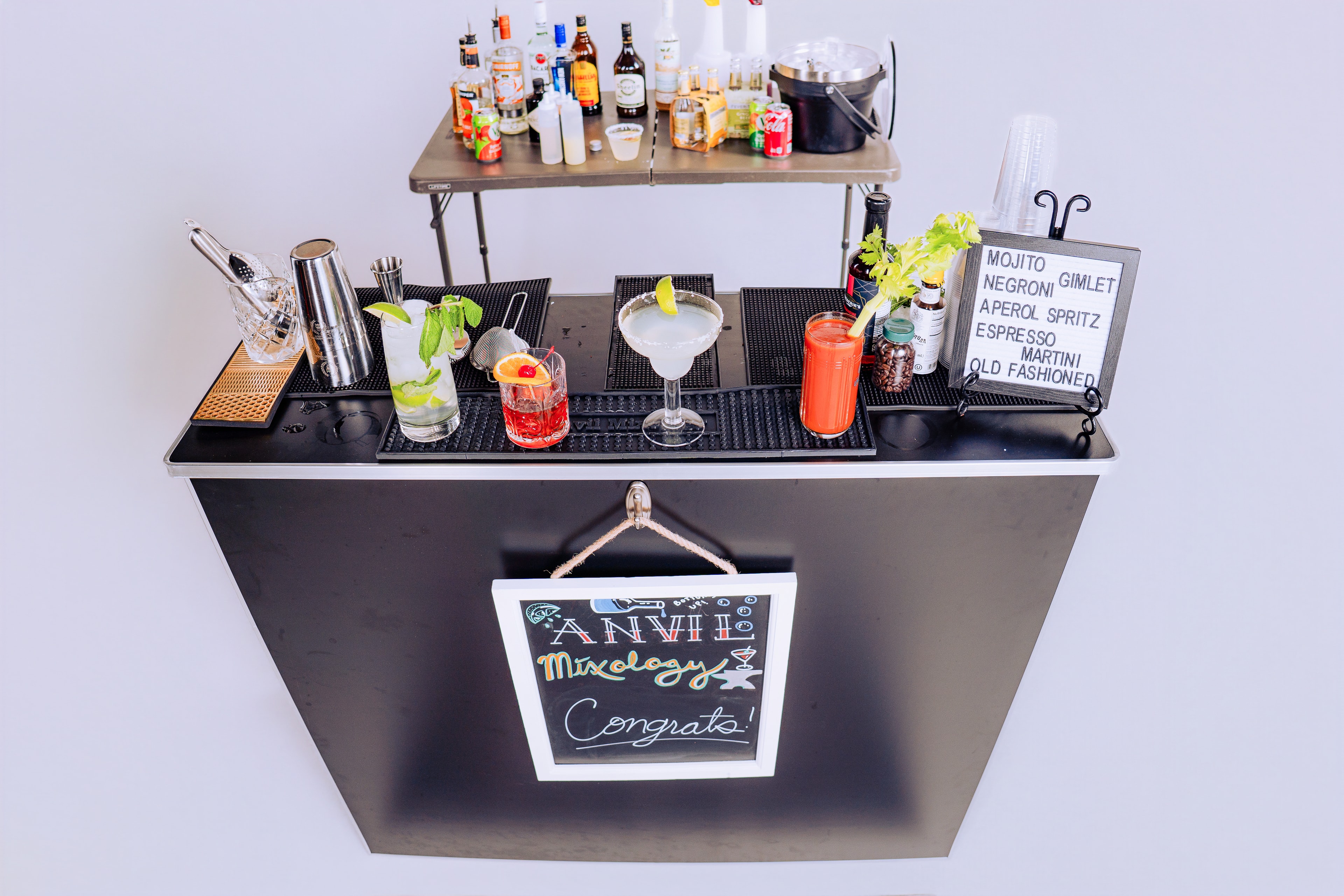 Anvil Mixology MKE full bar setup with cocktails and chalkboard sign