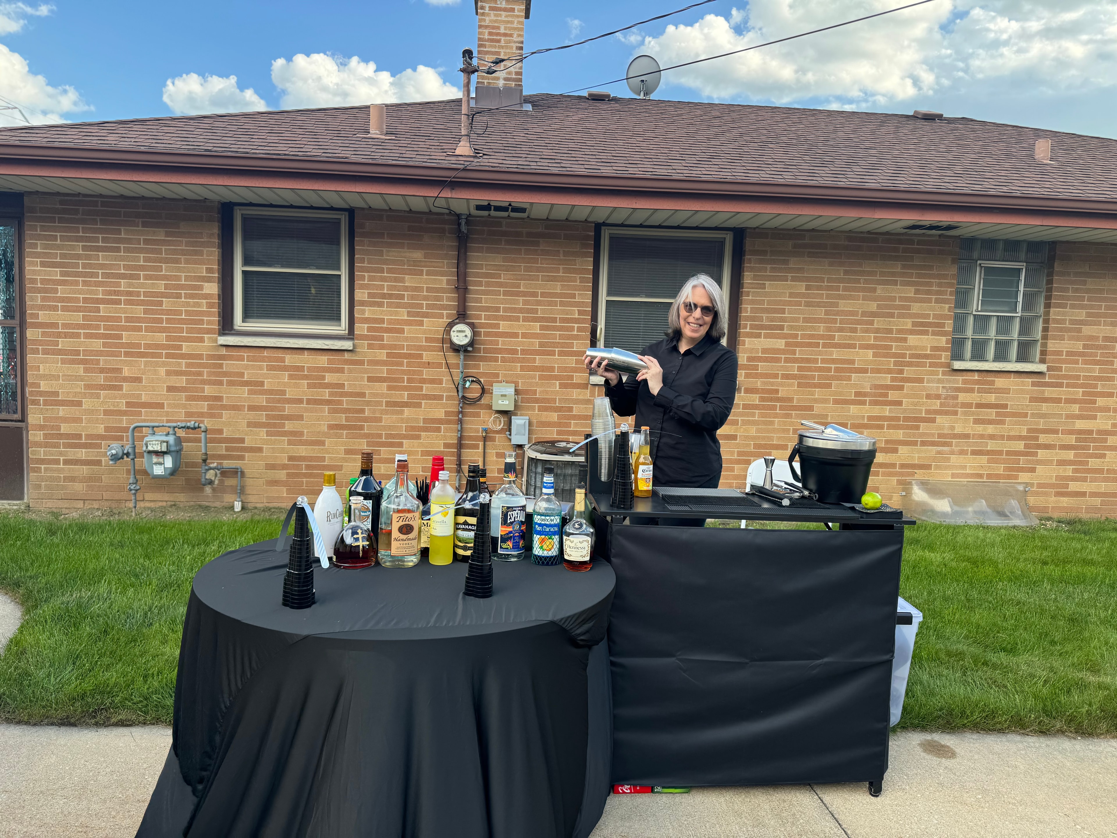 Desirae shaking cocktails at an outdoor bar setup with full spirit selection at a Cudahy housewarming